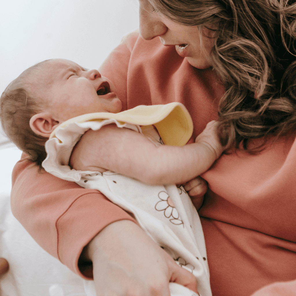 un bébé pleure dans les bras de sa maman qui essaie de le rassurer
